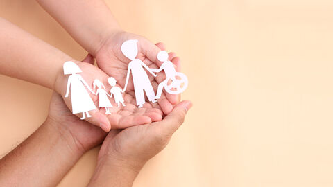 Zwei Personen halten gemeinsam einen Scherenschnitt in den Händen, der eine Familie darstellt. Zwei Personen halten gemeinsam einen Scherenschnitt in den Händen, der eine Familie darstellt.
